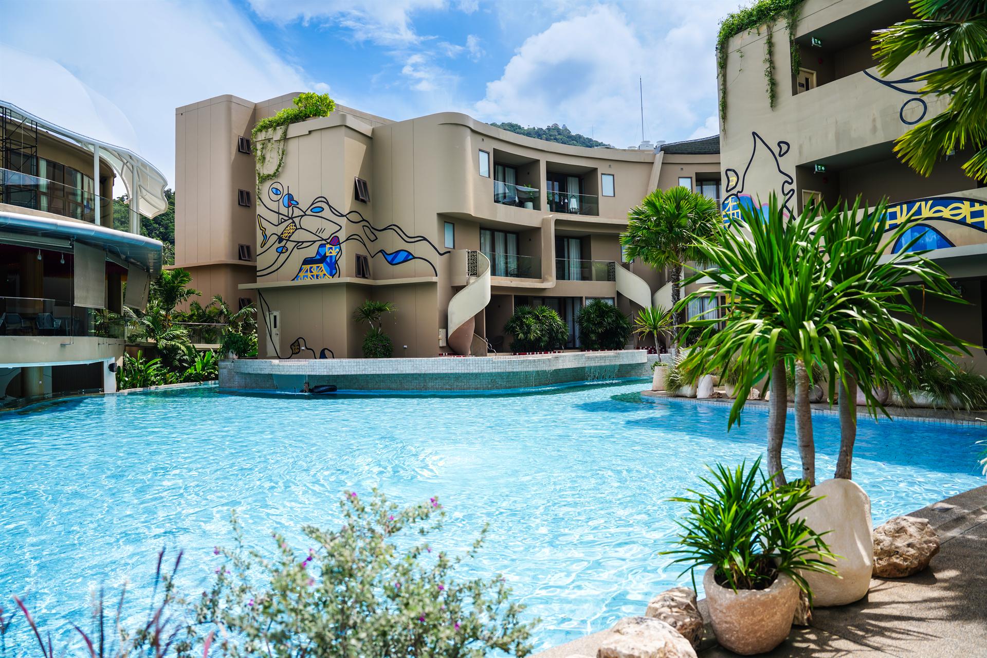 Daytime swimming pool surrounded by palms and contemporary buildings at Metadee Phuket