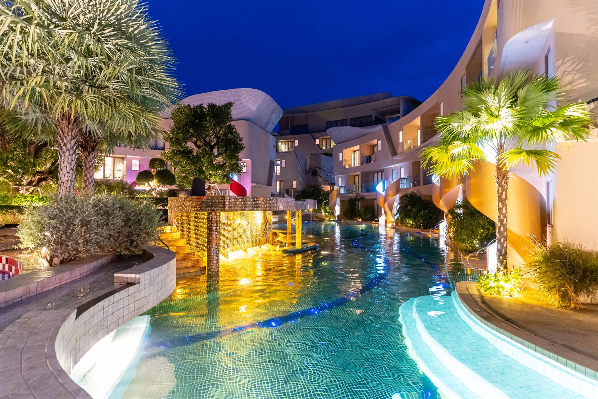 Illuminated swimming pool and palm trees at Metadee Concept Hotel in Phuket at night